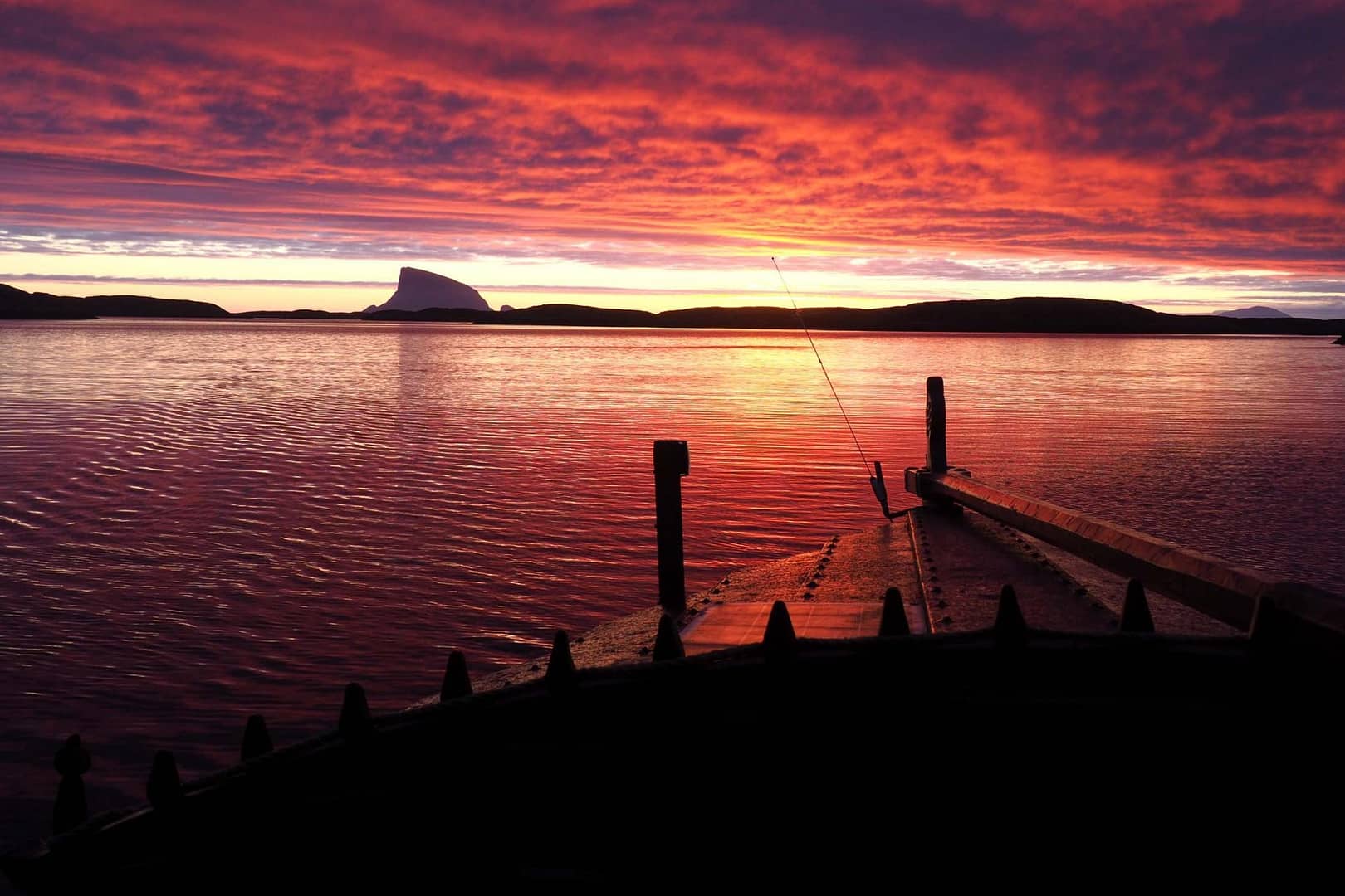 Seiling i solnedgang pa helgelandskysten. Trebat med rorgrind i forgrunnen, Lovund i bakgrunnen.