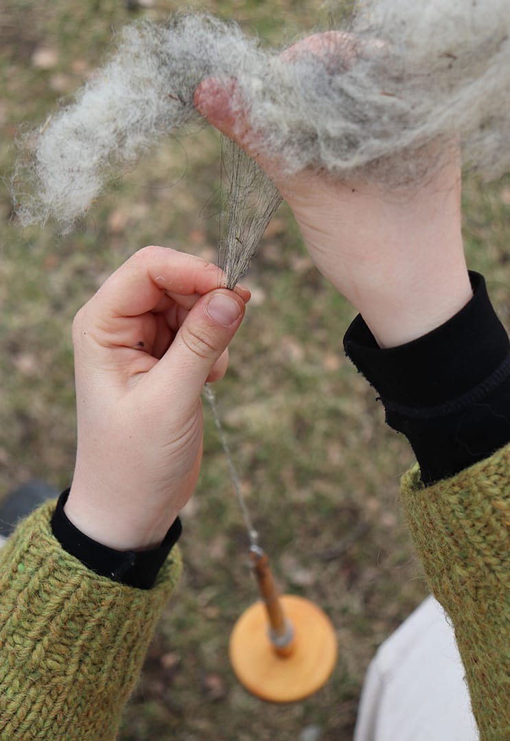 student learning to spin yarn on a traditional drop spindle